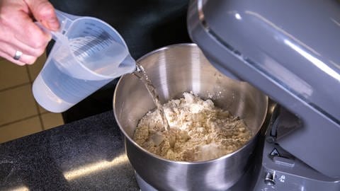 Wasser wird in eine Rührschüssel mit Mehl und Hefe geschüttet: Der Hefeteig für den Kassler im Brotteig muss laut Rezept gründlich verrührt werden. (Foto: SWR, Corinna Holzer)