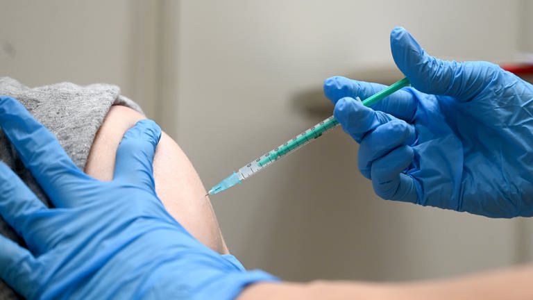 Eine Spritze mit Corona-Impfstoff wird in einem Oberarm gespritzt